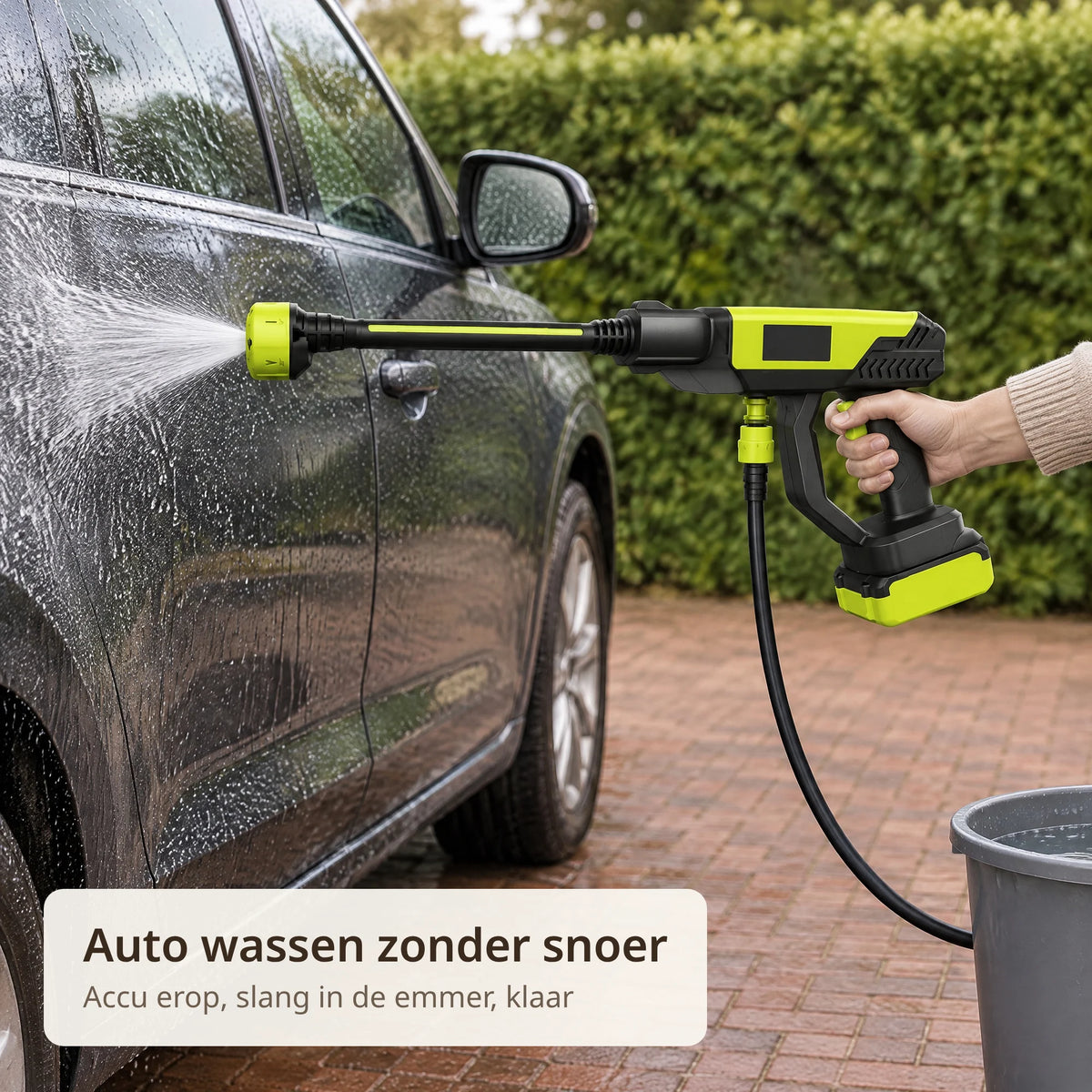 Draadloze accu hogedrukreiniger spuit een donkere auto af op de oprit, de slang loopt naar een emmer water