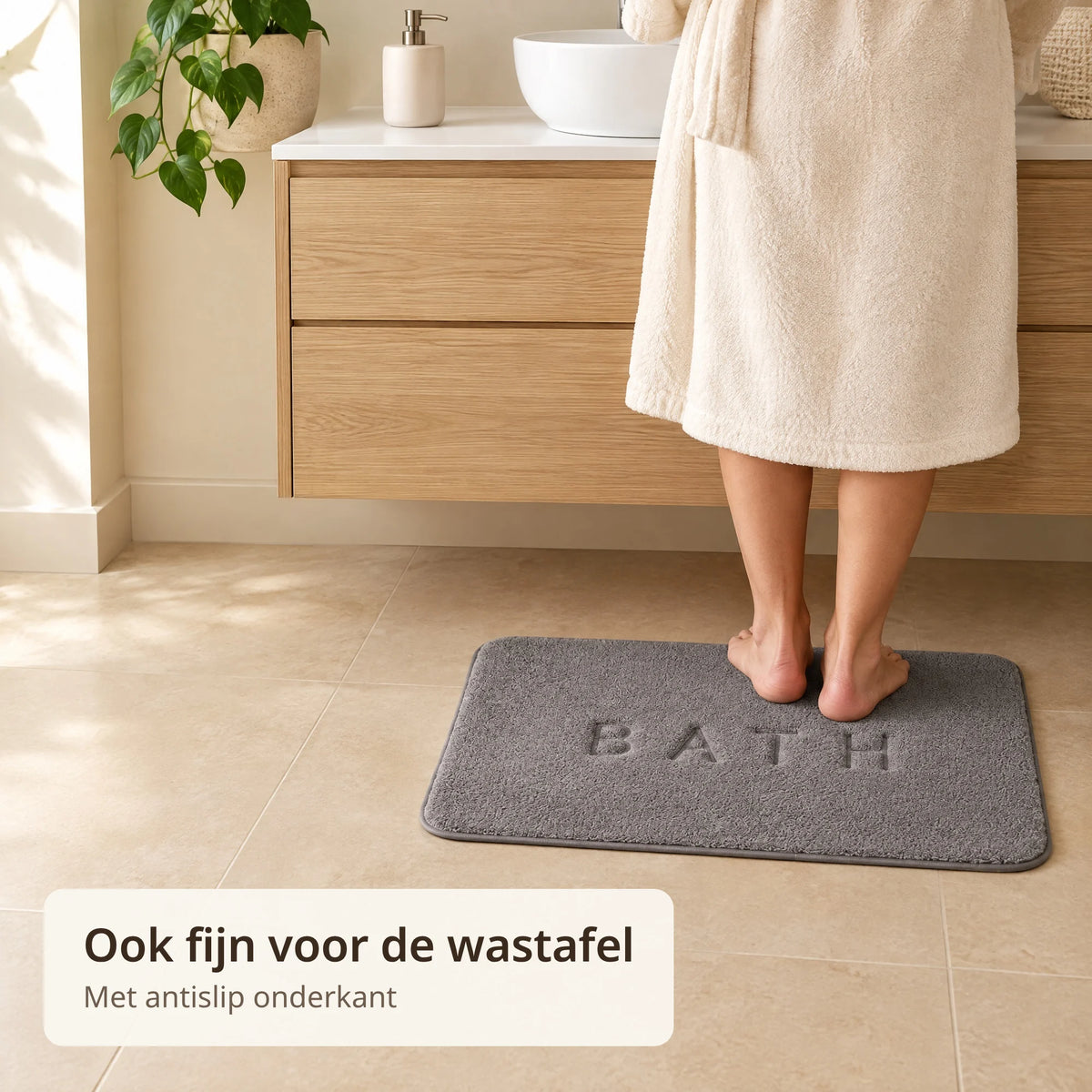 Persoon in badjas staat op blote voeten op de grijze antislip badmat voor een eiken wastafelmeubel
