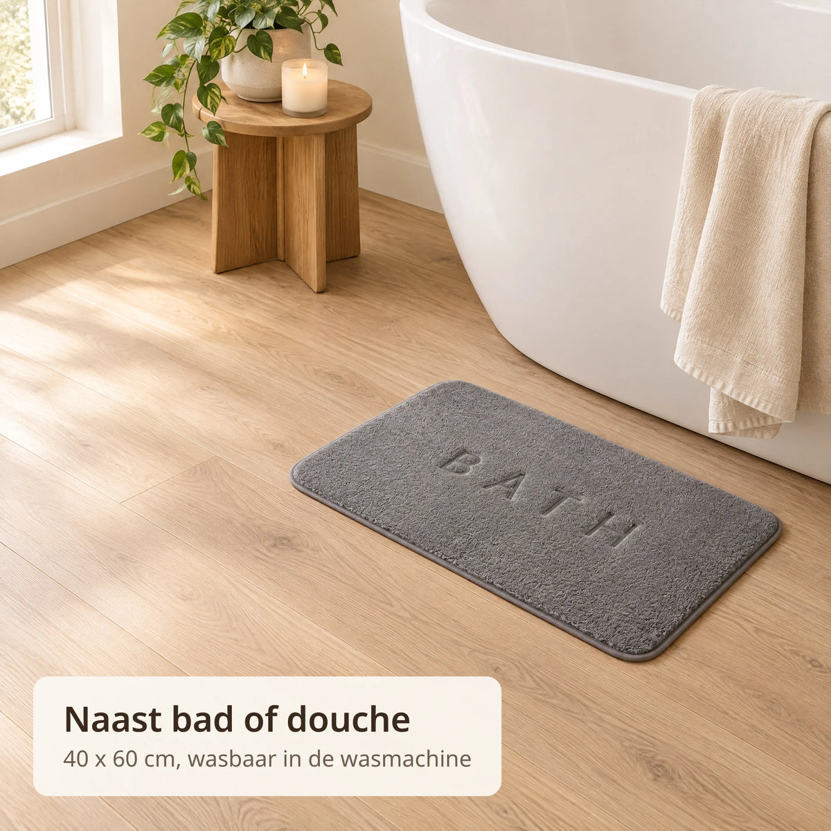 Grijze badmat van 40 x 60 cm ligt naast een vrijstaand wit bad op een houten vloer