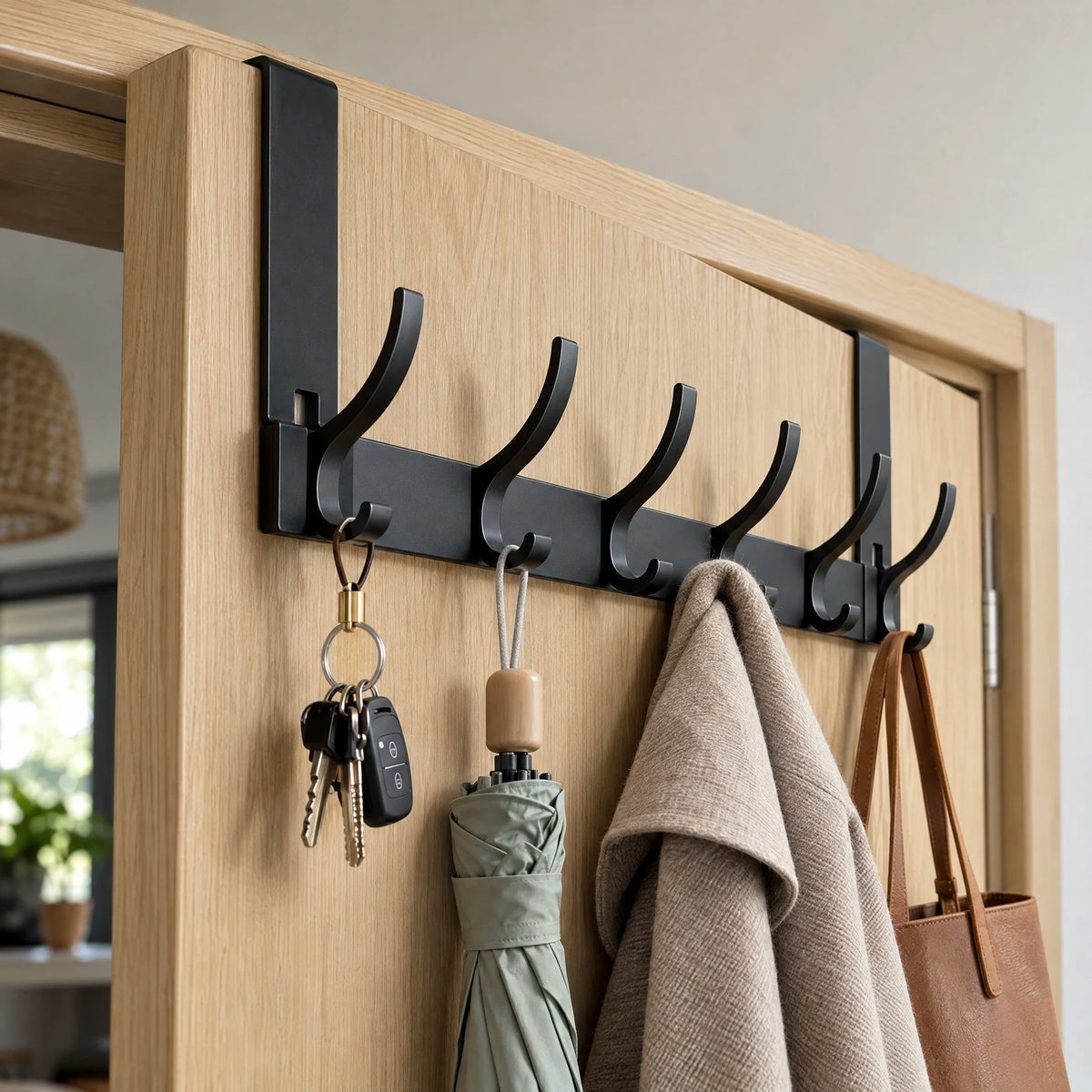 Zwarte deurhanger met haken over een houten deur met jas en tas