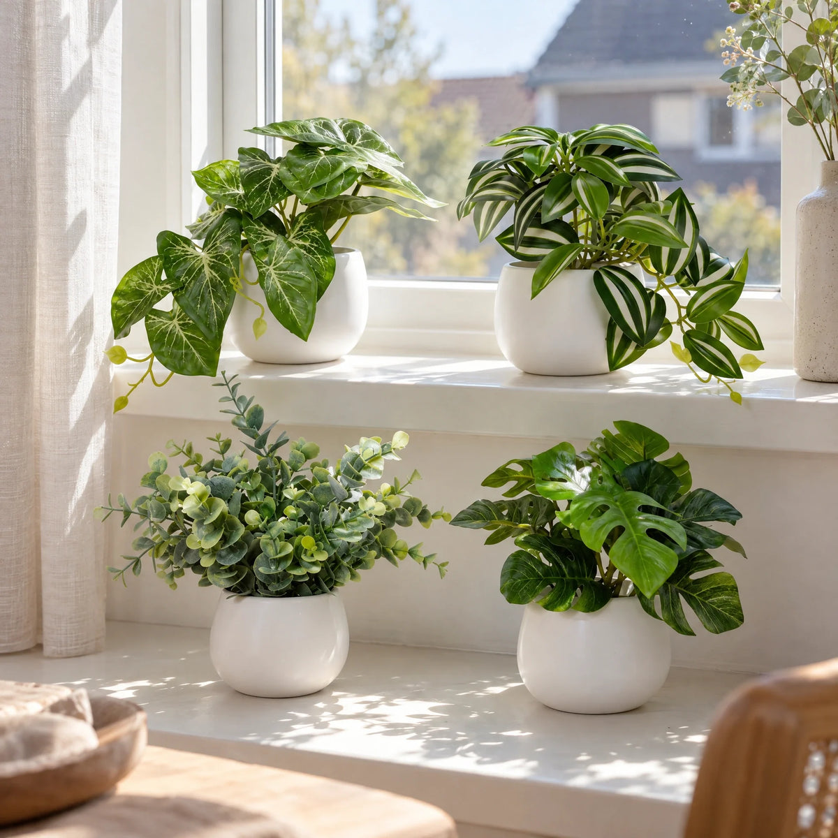 Vier kunstplanten in witte potjes op een vensterbank