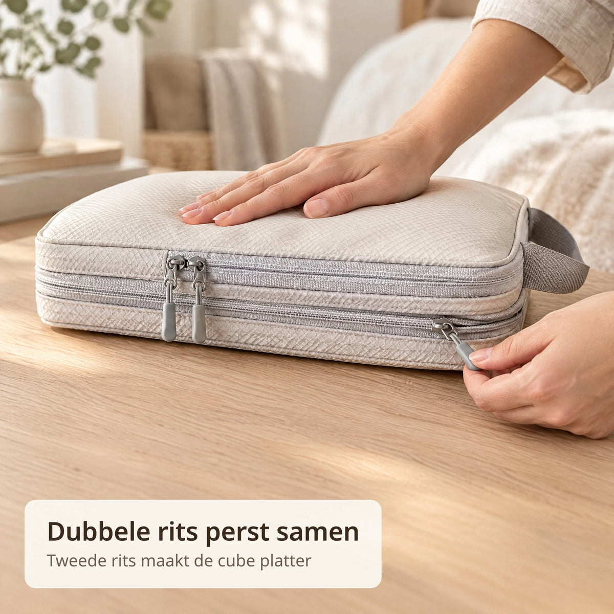 Hand trekt de tweede rits van een beige compressie packing cube dicht om hem platter te maken