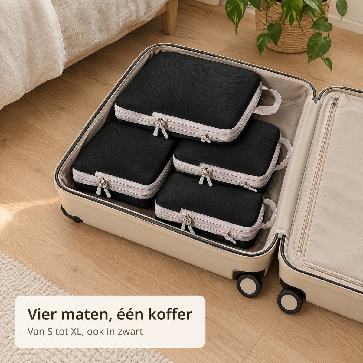 Vier zwarte packing cubes in verschillende maten liggen in een open koffer op een houten vloer