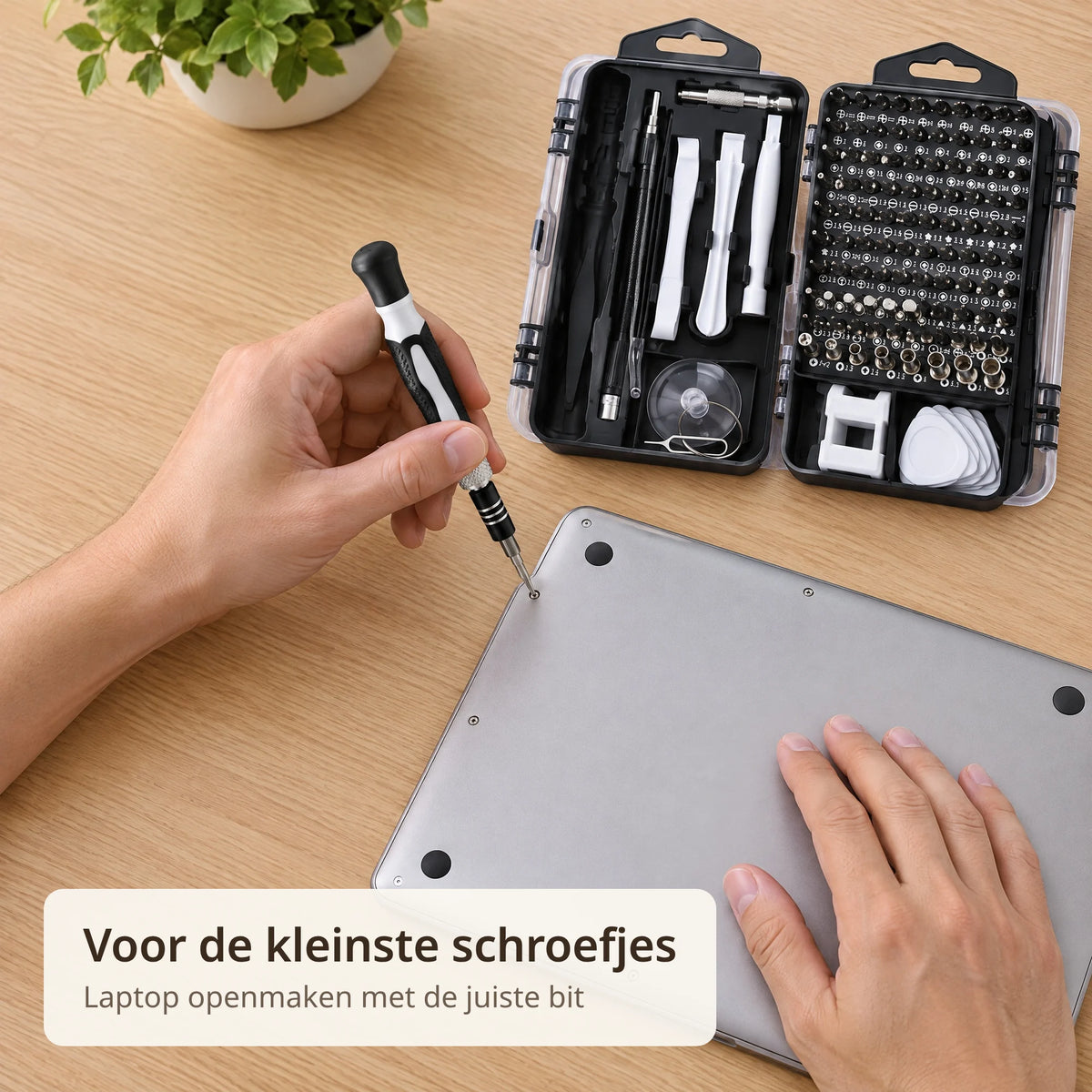Hand draait met de precisie schroevendraaier een schroefje los uit de onderkant van een laptop, de opengeklapte zwarte case met witte hulpstukken ligt ernaast