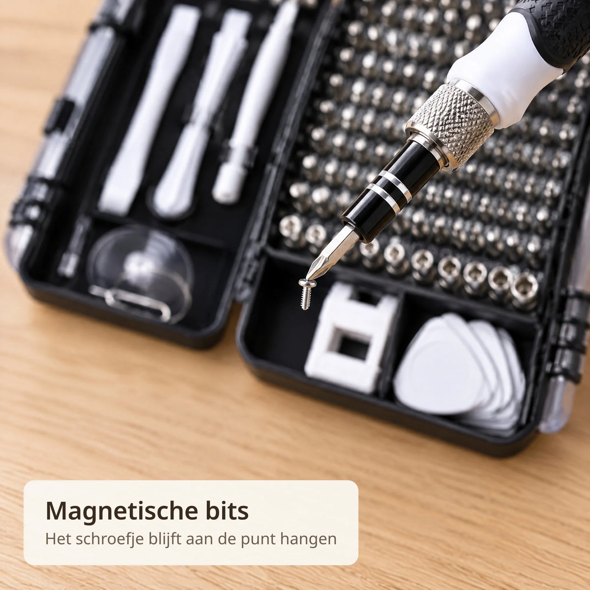Close-up van de magnetische bit van de precisie schroevendraaier met een schroefje aan de punt, boven de case met bitrek en witte hulpstukken