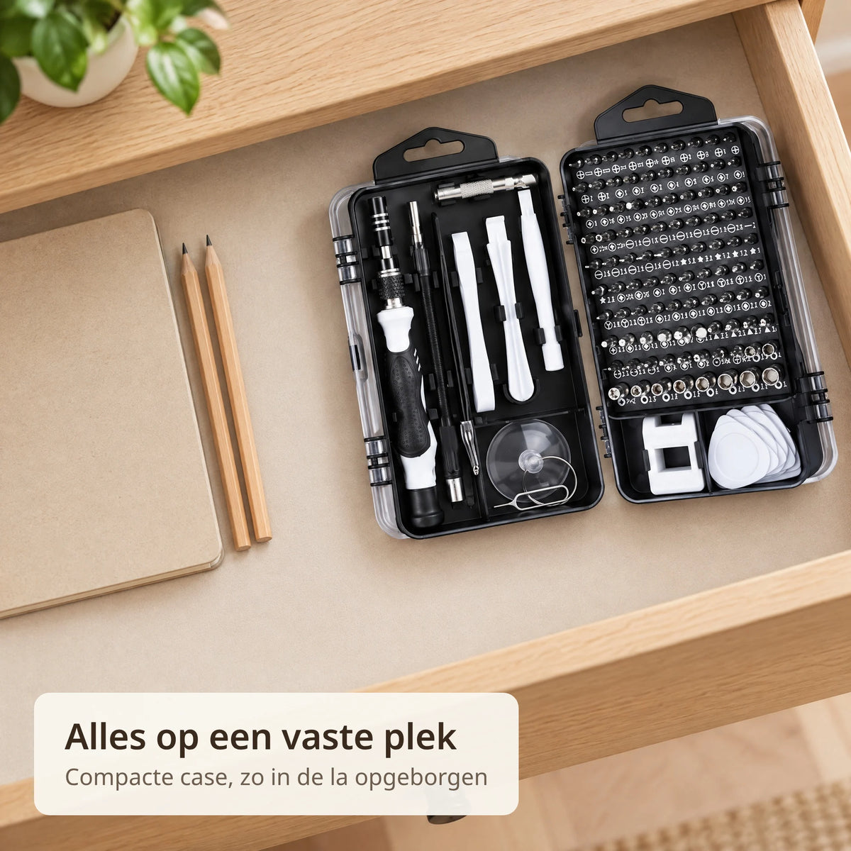 Precisie schroevendraaierset ligt opengeklapt in een bureaula naast een notitieboek en twee potloden, alle delen op hun plek in de zwarte case