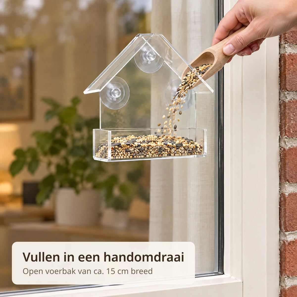 Hand vult de open voerbak van het raamvoederhuisje met vogelzaad uit een houten schepje