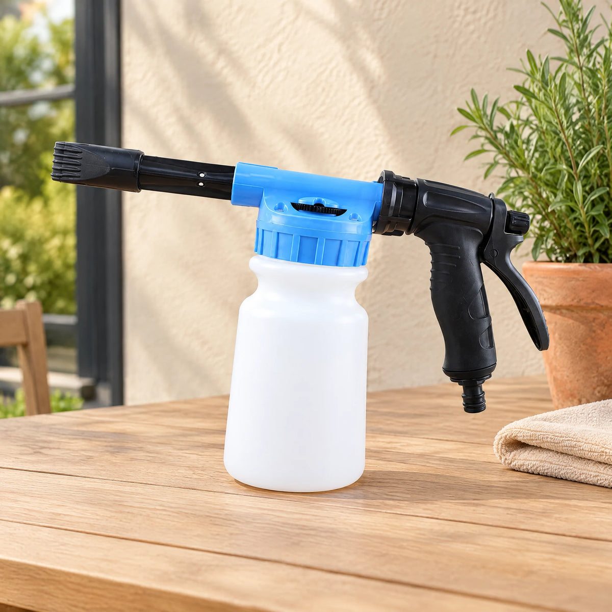 Schuimpistool voor de tuinslang met blauwe mengkop, zwarte handgreep en witte fles van 1 liter op een houten tuintafel