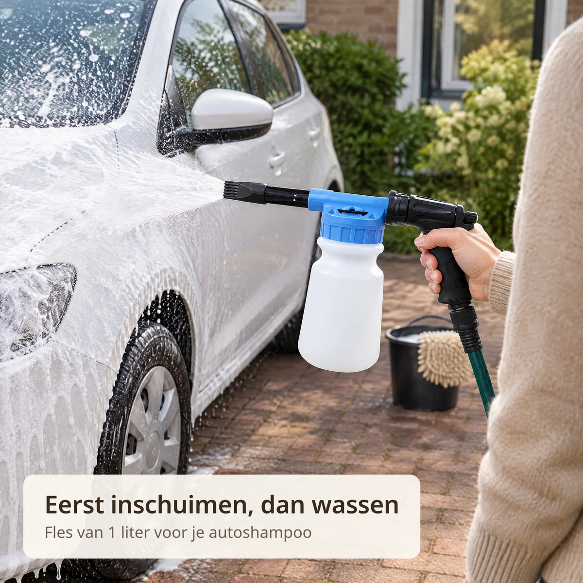 Witte auto wordt op de oprit ingeschuimd met de schuimsproeier aan de tuinslang