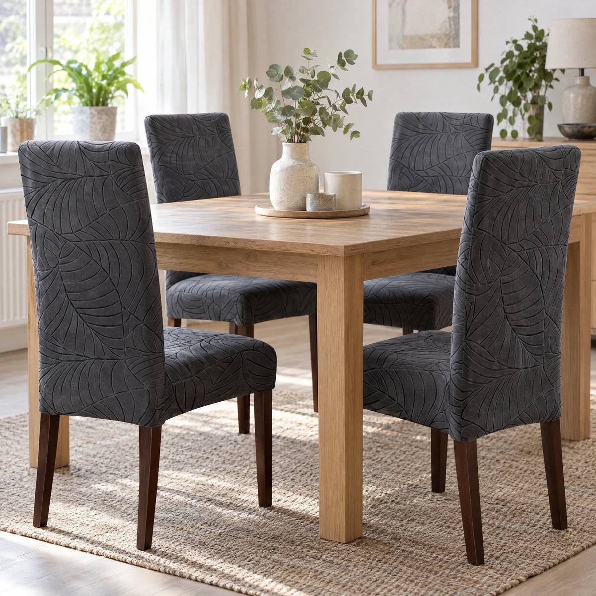 Vier eetkamerstoelen met donkergrijze stretch hoezen aan een eikenhouten tafel