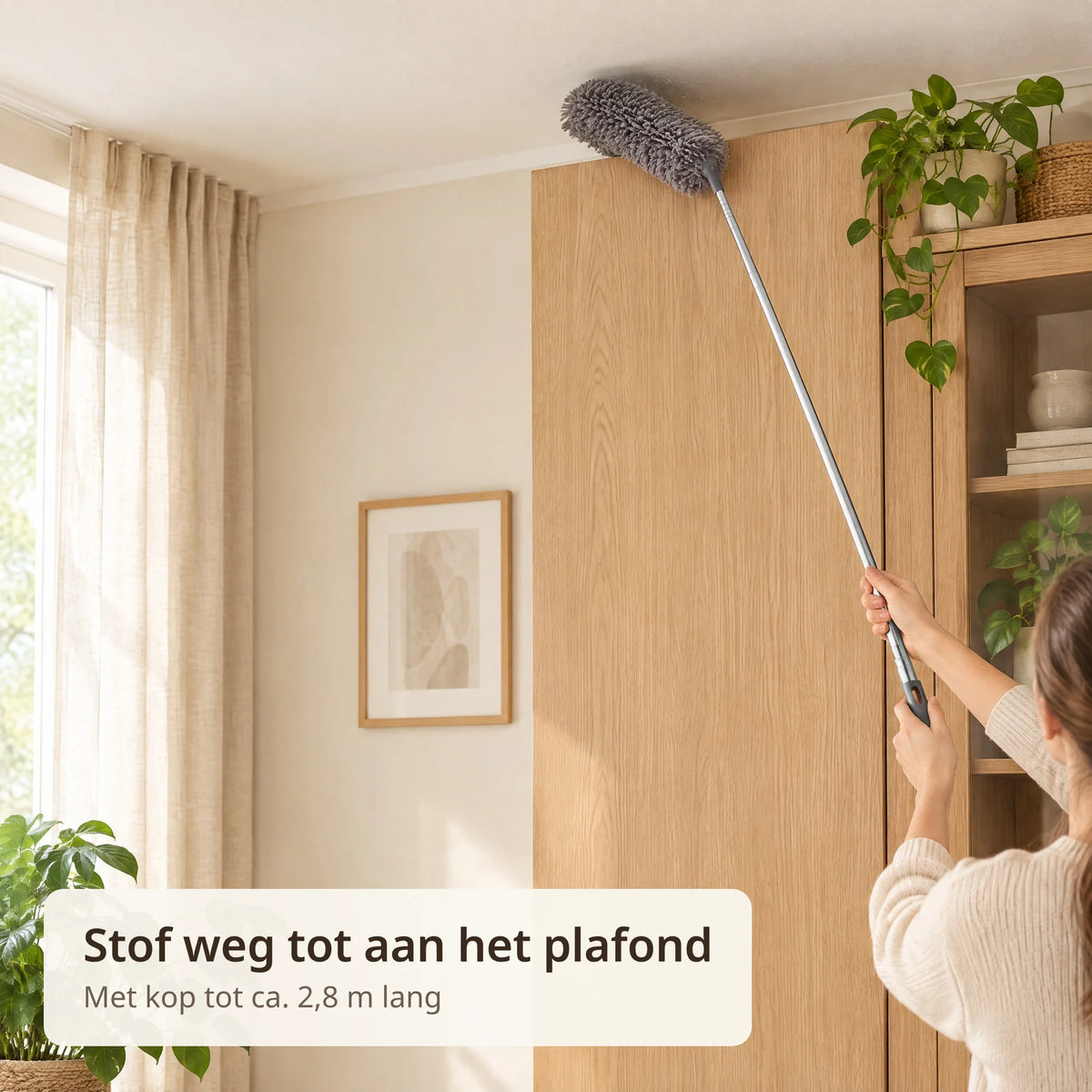 Uitgeschoven telescopische plumeau met pluizige grijze kop stoft de bovenkant van een hoge kast af