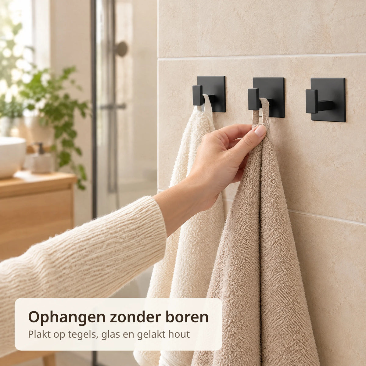 Hand hangt een handdoek aan een zwarte zelfklevende handdoekhaak op een tegelwand in de badkamer