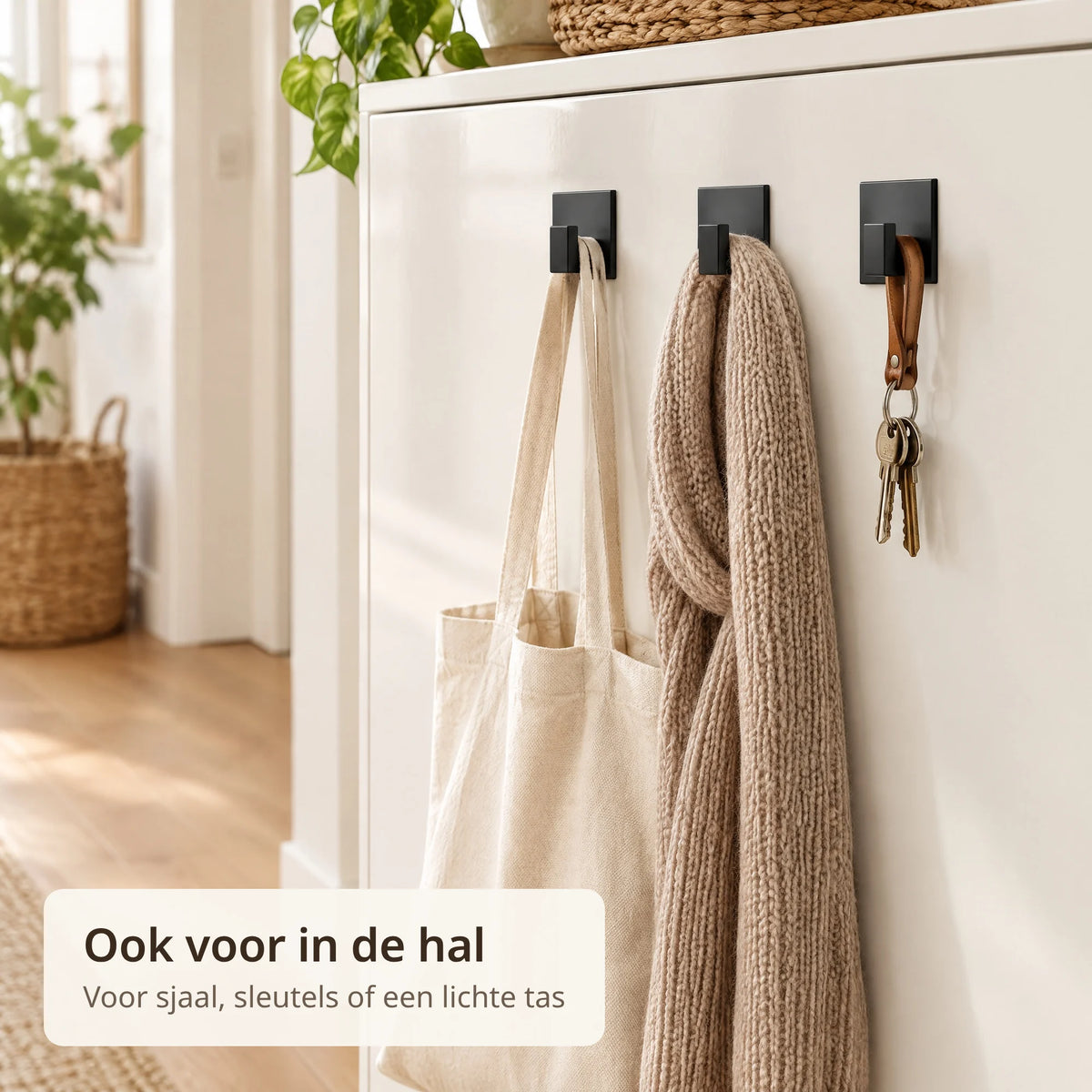 Drie zwarte zelfklevende haken op een gelakt kastpaneel in de hal met een katoenen tas, een sjaal en sleutels