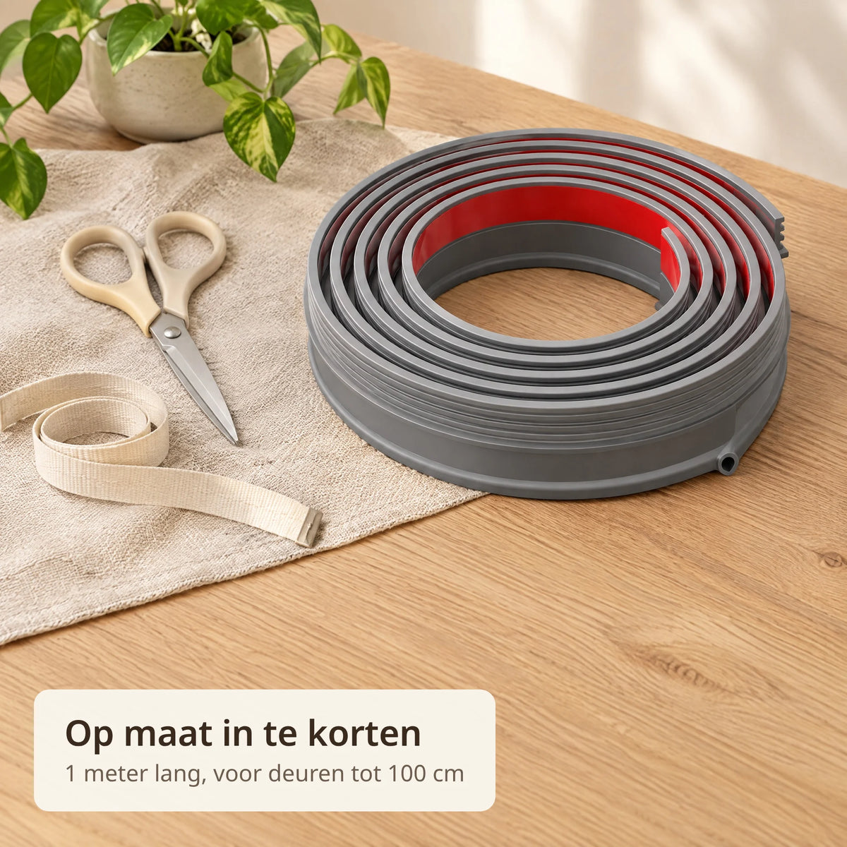 Opgerolde grijze tochtstrip met rode beschermfolie naast een schaar en meetlint op een eiken tafel